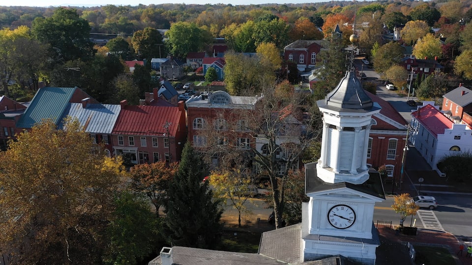 A town with a prominent clock tower, red-roofed buildings, and autumn-colored trees.