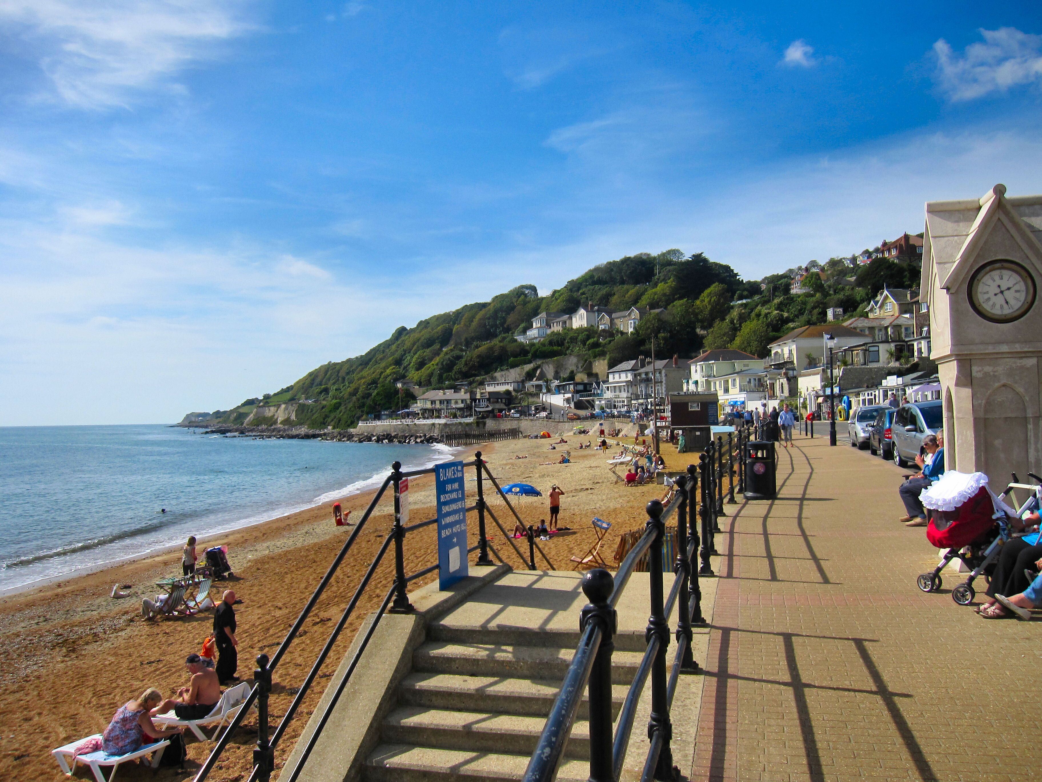 A beach with people sunbathing, a clock tower, and houses on a hillside.