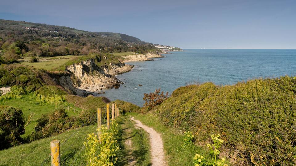 A coastal path with cliffs, a beach, and a distant town.