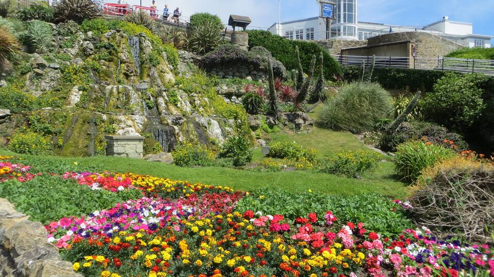 A hillside garden with colorful flowers, a red tram, and a white building with a tower.
