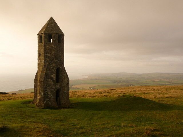 A solitary stone tower on a grassy hill with a cloudy sky in the background.