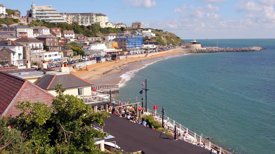 A coastal town with a beach, promenade, and buildings along the hillside.