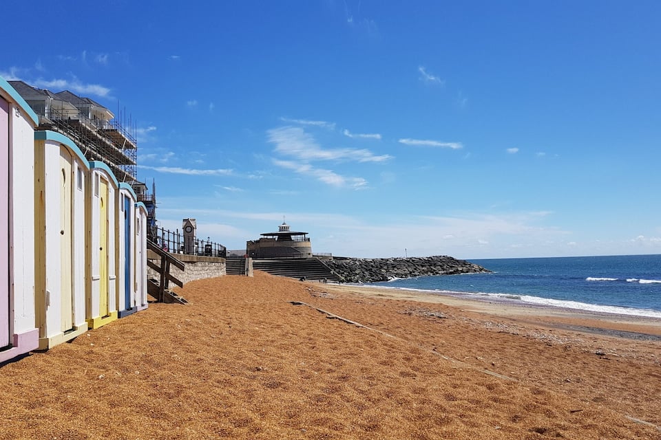 Une plage bordée de cabanes colorées, d’un phare et de brise-lames rocheux.