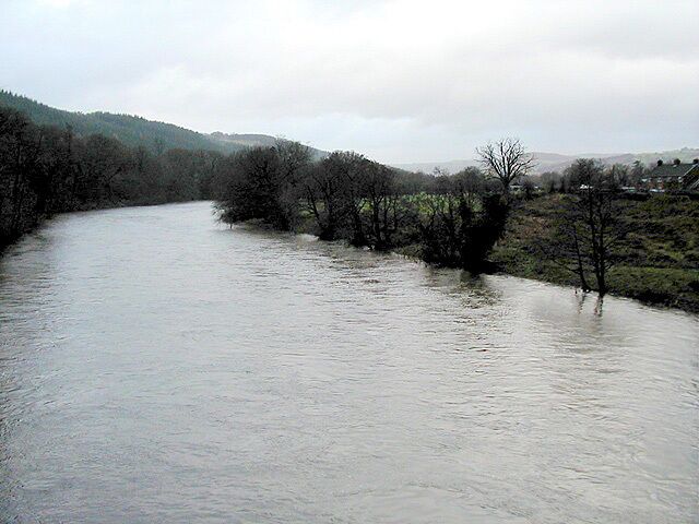 A river flowing through a valley with trees on both sides and hills in the background.