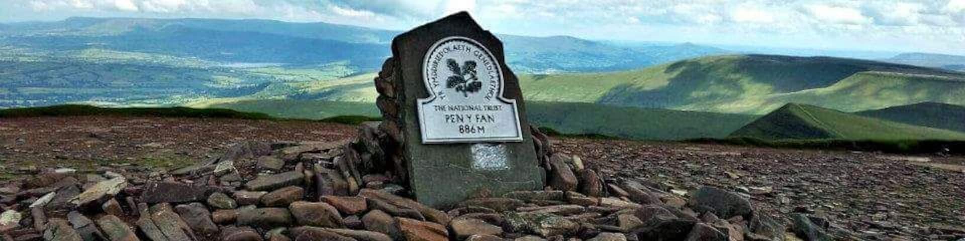 Un montículo de piedras con una placa en un promontorio rocoso, con vistas a colinas ondulantes al fondo.