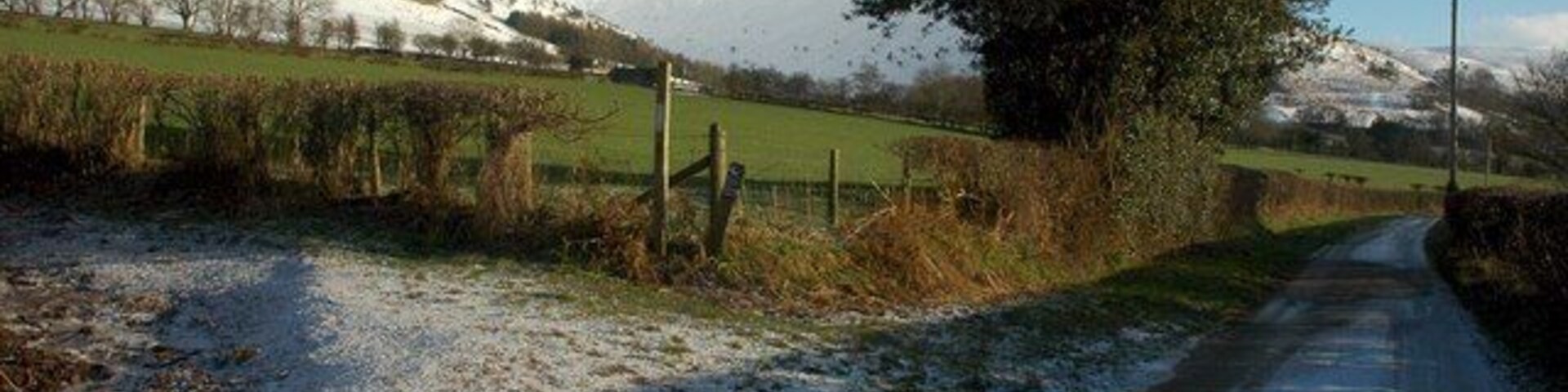 Un camino rural cubierto de nieve con una cerca y árboles a los lados.