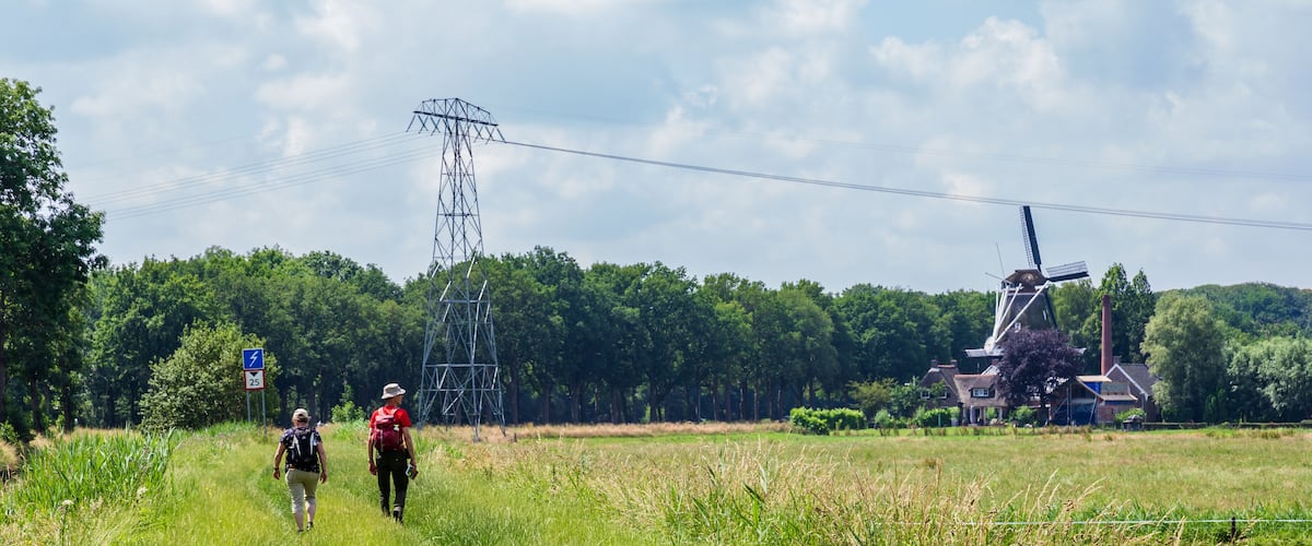 A rural landscape with a power line tower, a windmill, and a house.