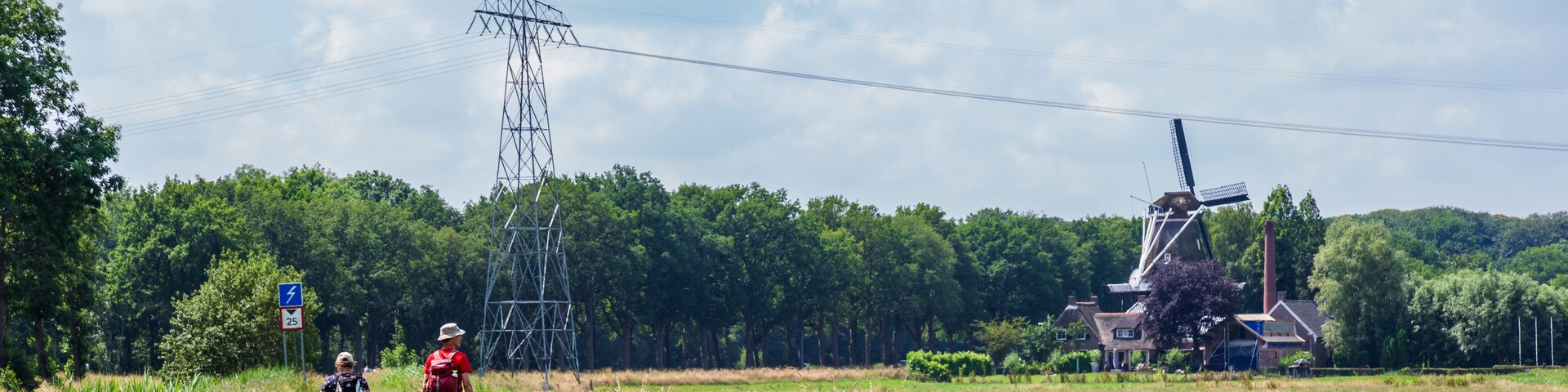 A rural landscape with a power line tower, a windmill, and a house.