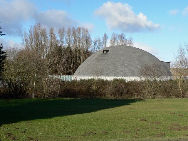 Un edificio grande de forma abovedada rodeado de árboles y un campo cubierto de césped.