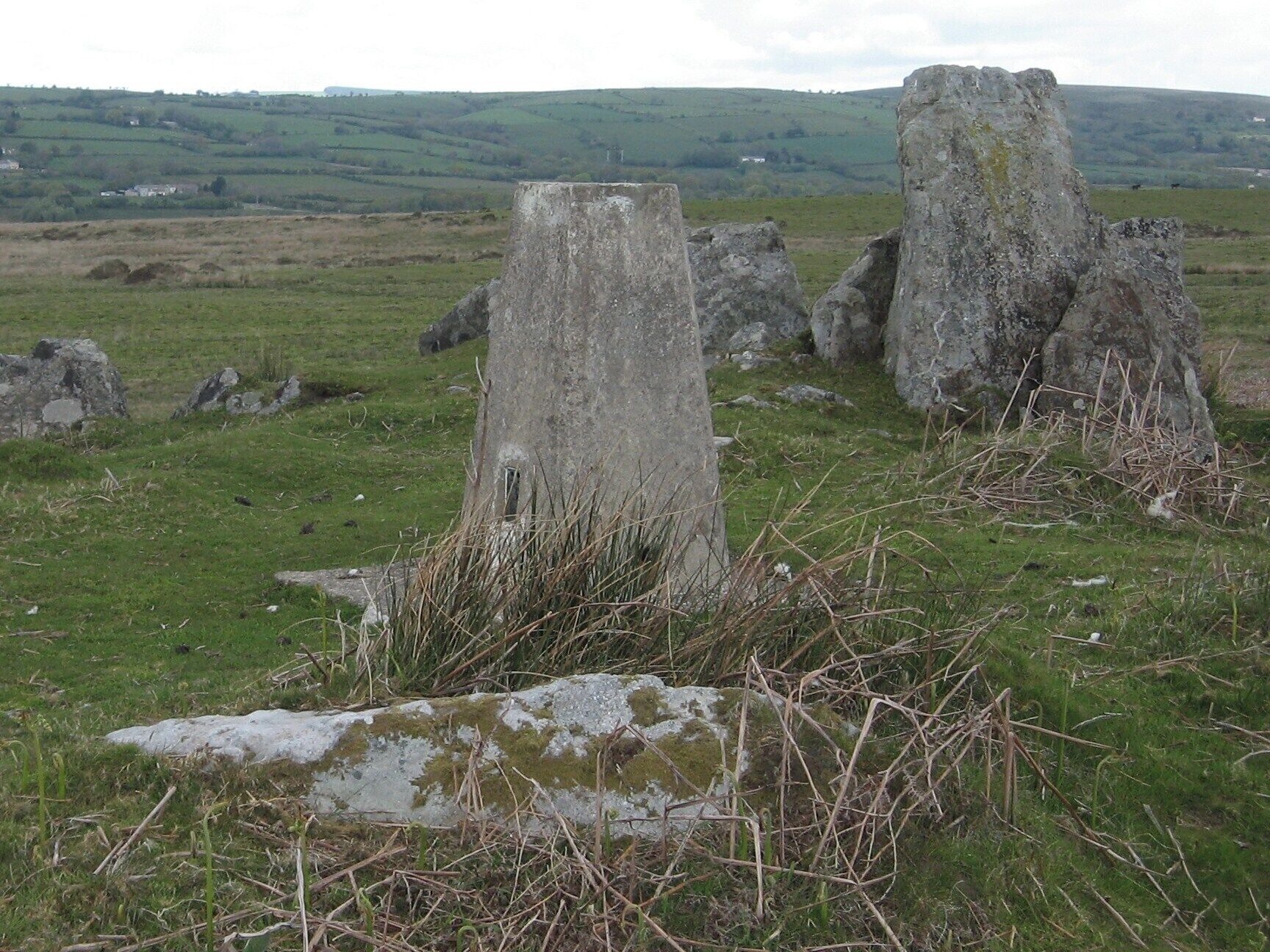 Una construcción de piedra en un campo cubierto de hierba, con colinas onduladas al fondo.