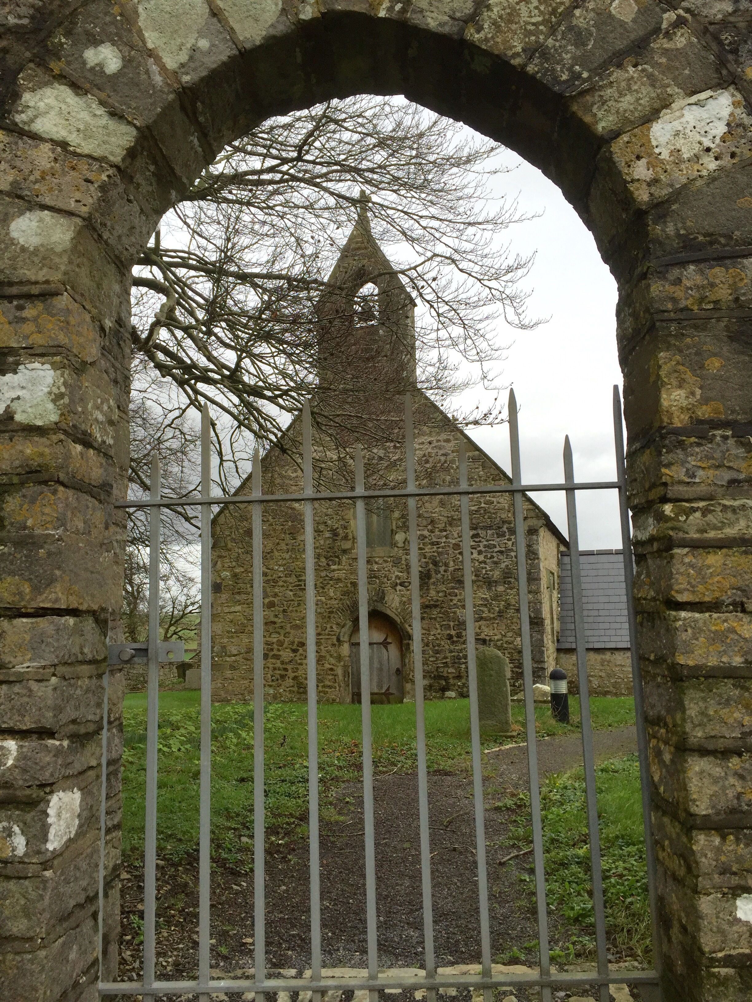 An arched stone gateway leading to a stone building with a pointed roof.