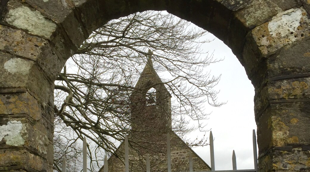 An arched stone gateway leading to a stone building with a pointed roof.