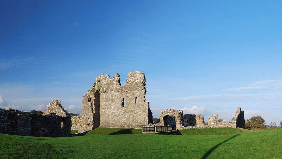 The ruins of a medieval castle with a grassy hill and a clear blue sky.