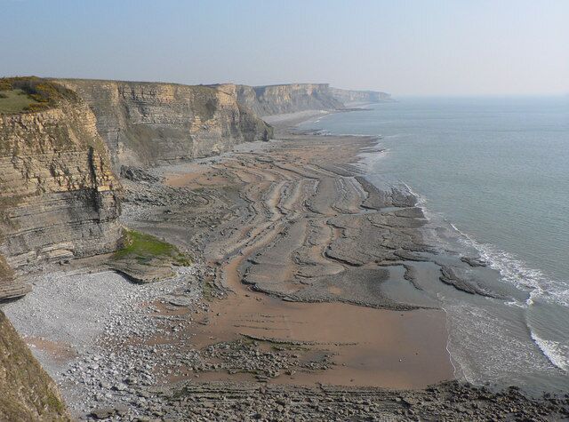A coastal landscape with cliffs, a sandy beach, and a calm sea.