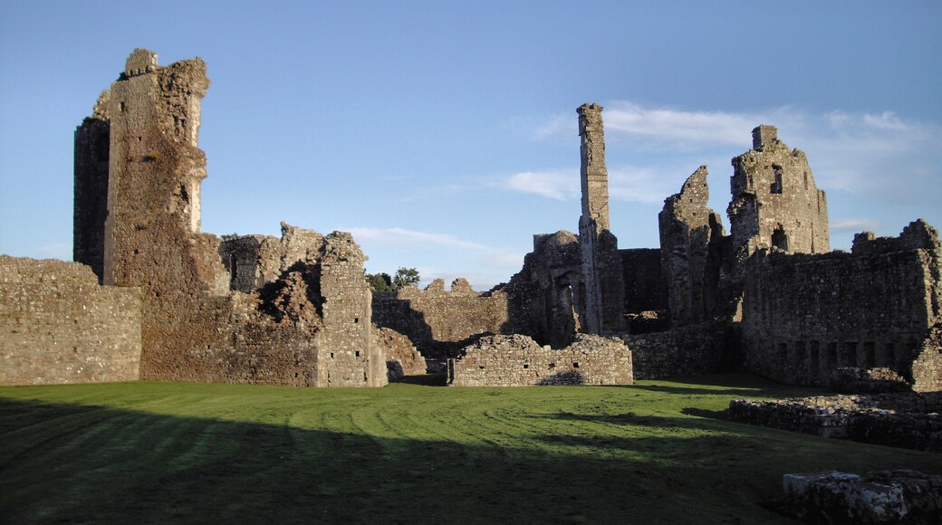 Las ruinas de un castillo medieval, con altas y deterioradas murallas y un patio cubierto de césped.