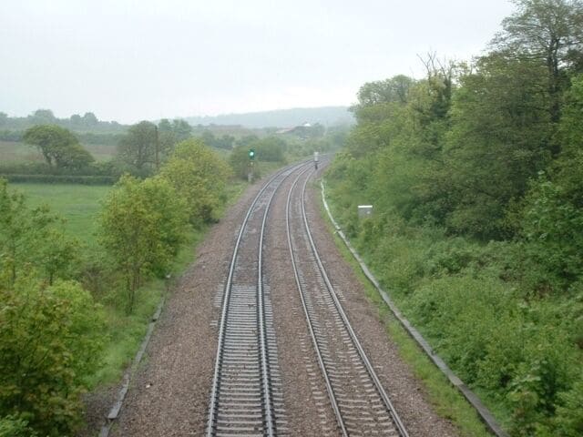 Railway tracks curving through a rural landscape with greenery on both sides.