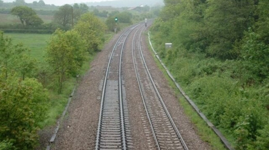 Railway tracks curving through a rural landscape with greenery on both sides.