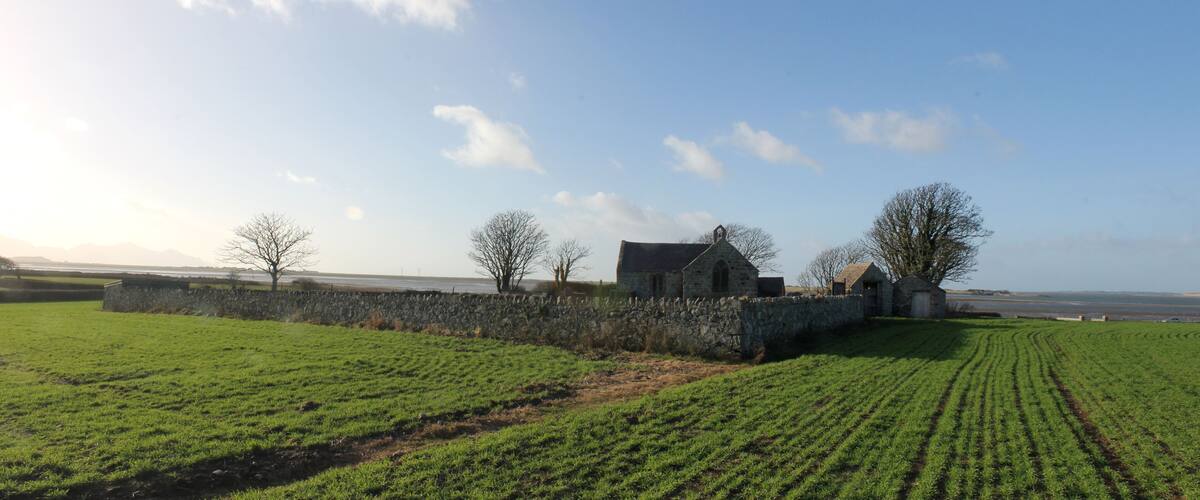 A rural landscape with a stone wall, a stone building, and a field of crops.
