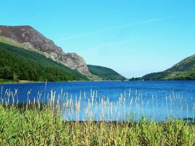 A lake surrounded by green hills and clear blue sky.