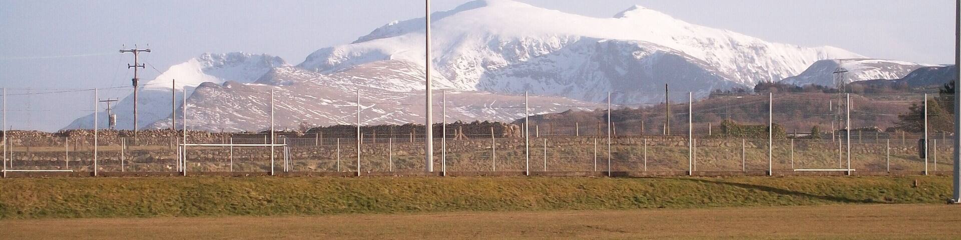 The Sports Field at Ysgol Brynrefail This is a field with a view. The snow covered peaks of Crib Goch, Carnedd Ugain and Yr Wyddfa (Snowdon) form the background.