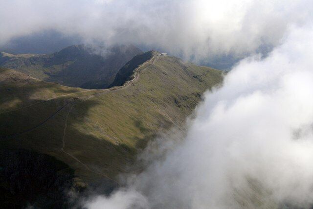 A mountain landscape with a winding path and clouds partially covering the peaks.