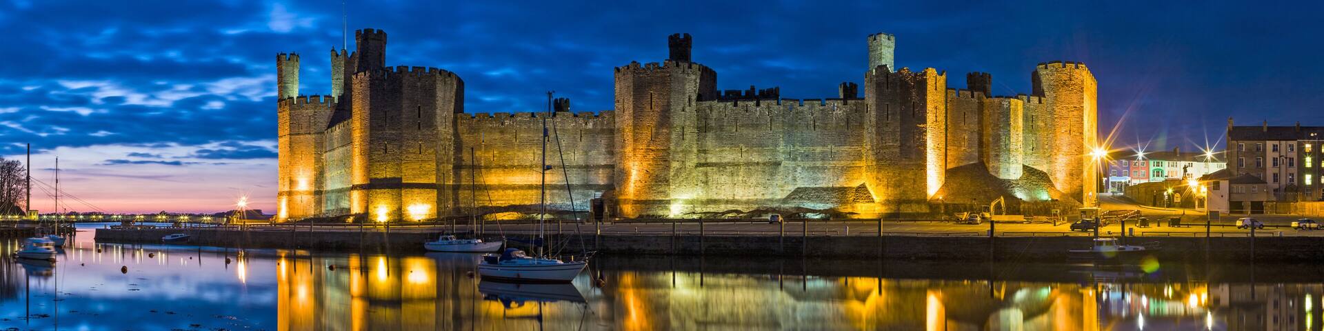 A historic castle with multiple towers and a moat, reflecting in the calm water.