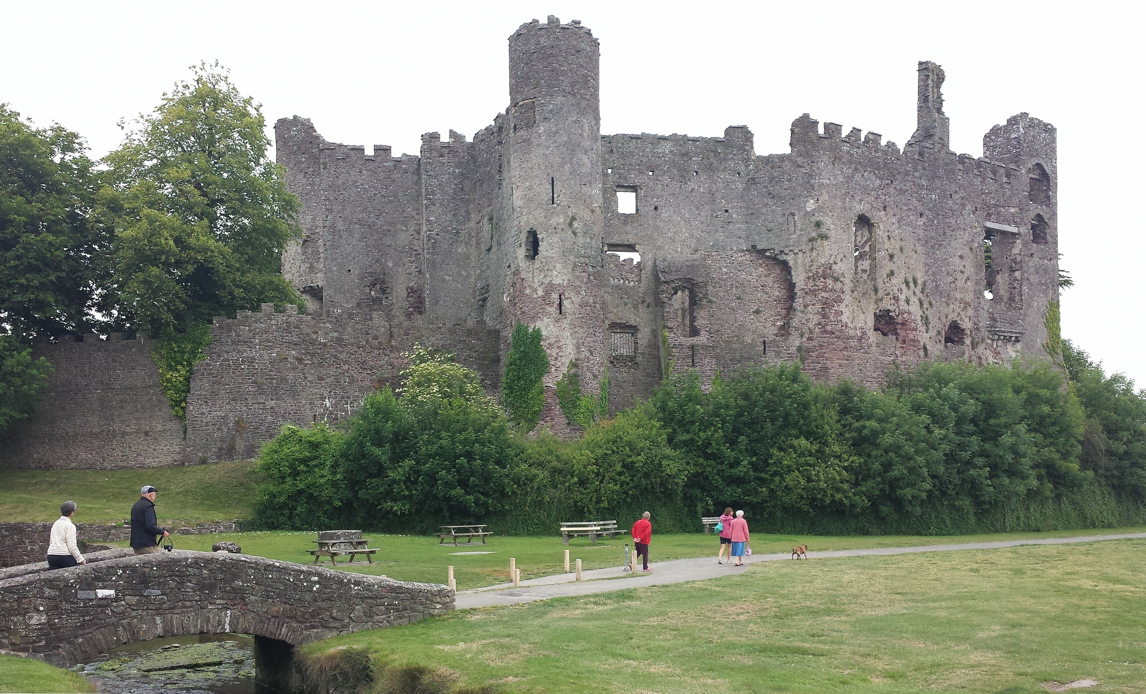 A historic castle with ruins, a stone bridge, and a grassy park with picnic tables.