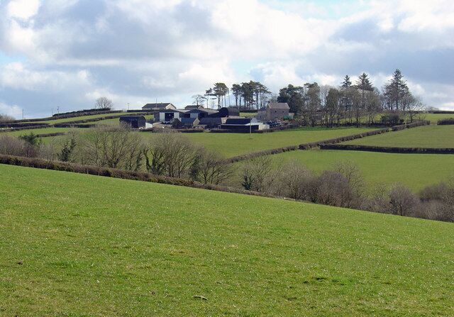 A rural landscape with rolling hills, green fields, and scattered farm buildings.
