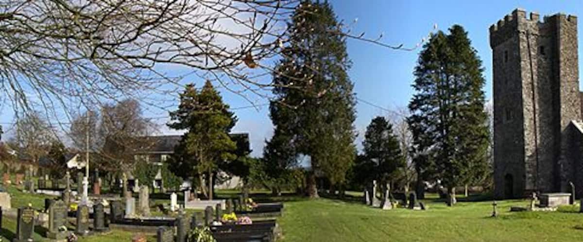 A church with a tall tower, surrounded by a cemetery with gravestones and trees.