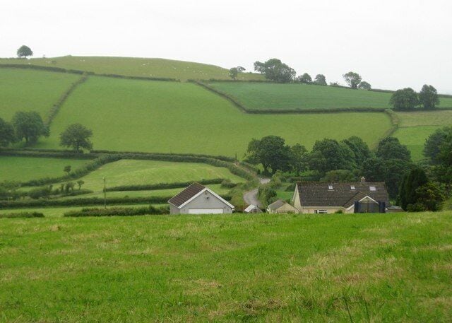 Rolling green hills, a white house, and a barn in a rural landscape.