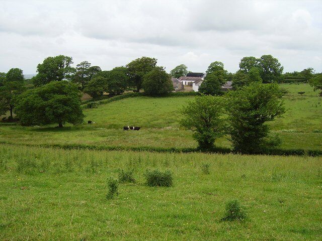 A grassy field with trees and a house in the background.