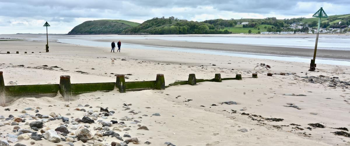 A sandy beach with scattered rocks, a person walking, and a distant hill with a castle-like structure.