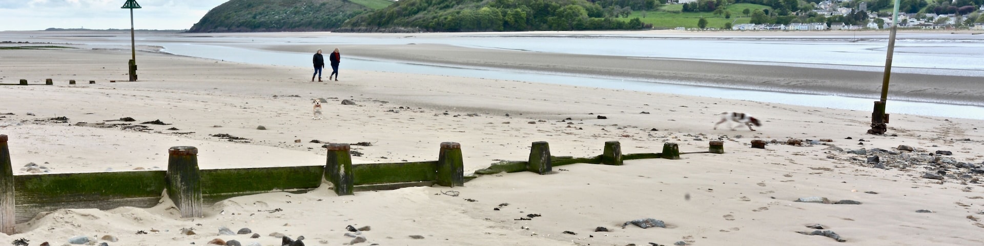 A sandy beach with scattered rocks, a person walking, and a distant hill with a castle-like structure.