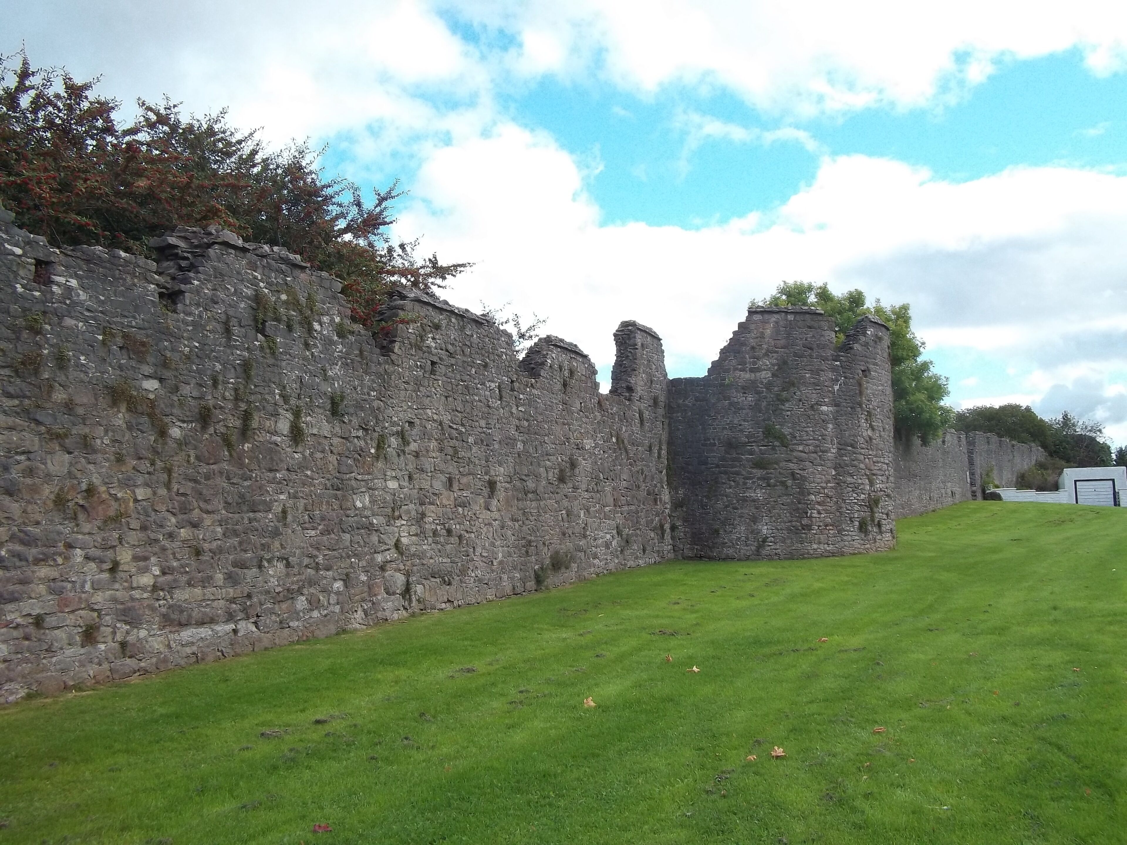 A stone wall with ruins and a grassy field.