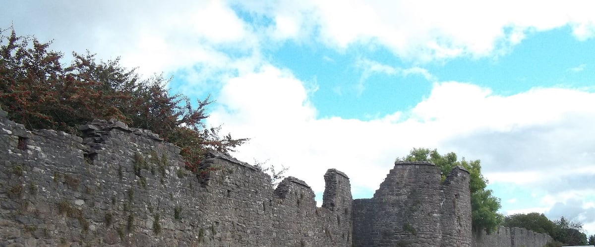 A stone wall with ruins and a grassy field.