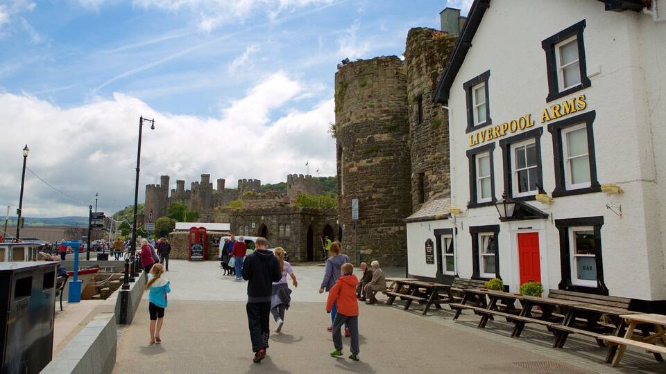 A historic castle in the background, a white building with 'LIVERPOOL ARMS' sign, and people walking in the foreground.