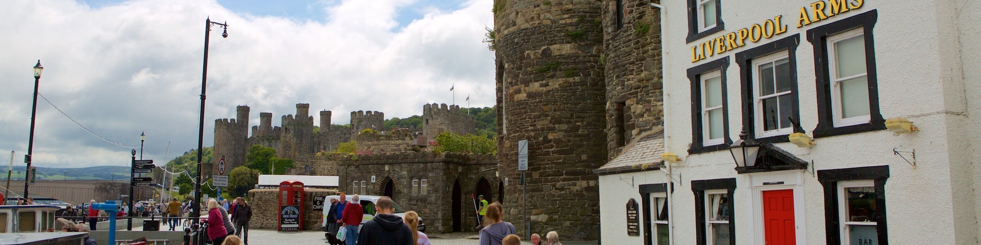 A historic castle in the background, a white building with 'LIVERPOOL ARMS' sign, and people walking in the foreground.