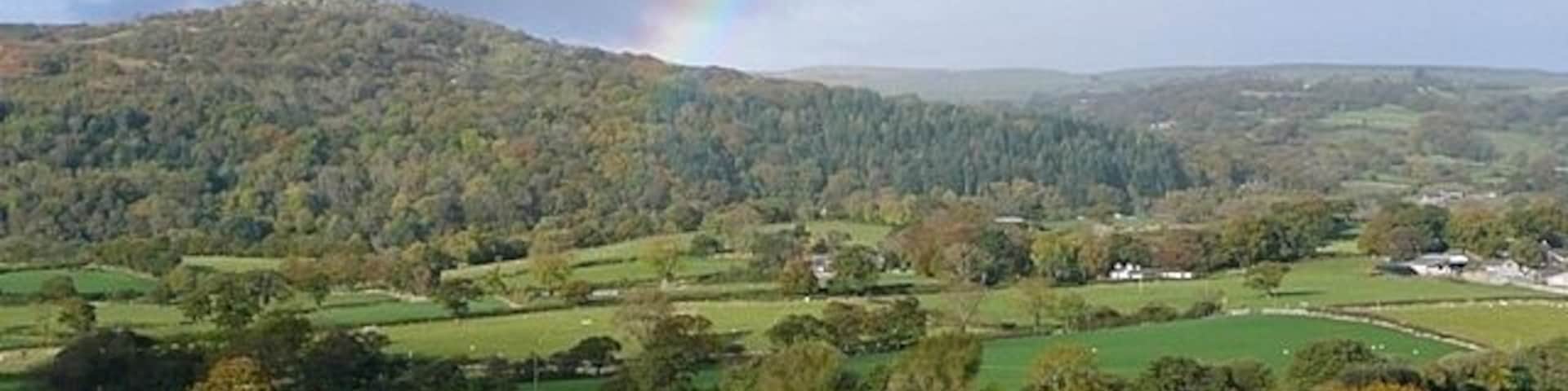 Farmland above Llangelynin As I left my friends' house near Conwy, travelling south, I saw this wonderful view framed by a rainbow. I have no idea where the rain was. In the background the wooded area of Parc Mawr leads to Craig Celynin in SH7473