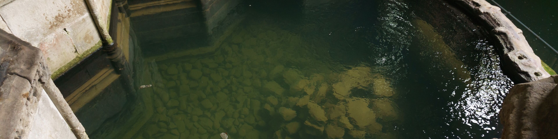 A stone pool with clear water, surrounded by stone walls and steps.