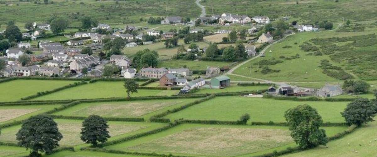 En landlig landsby med huse, marker og spredte træer.