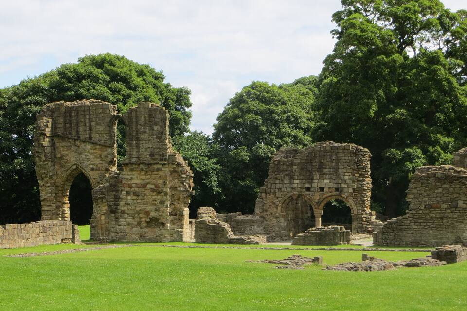 Ancient stone ruins with arches, surrounded by lush green grass and trees.