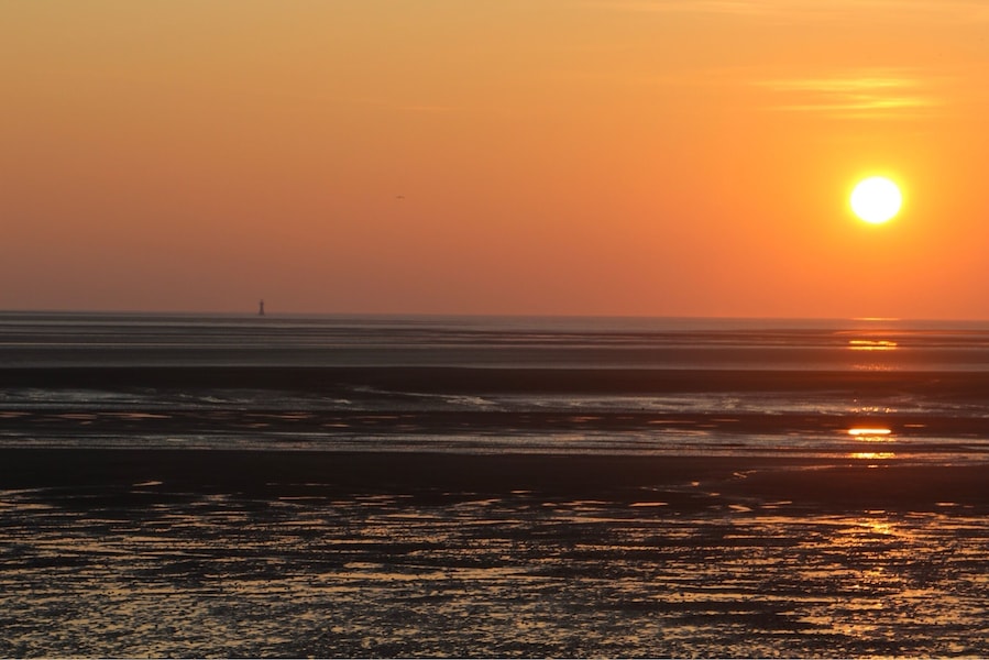 A sunset over a beach with waves and a distant lighthouse.