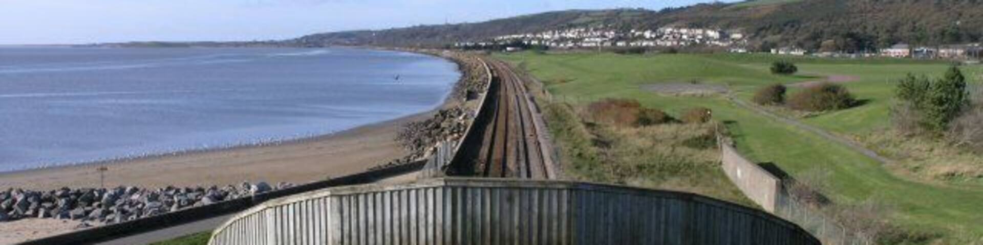 A coastal railway track curving along a beach with grassy fields and a distant town.