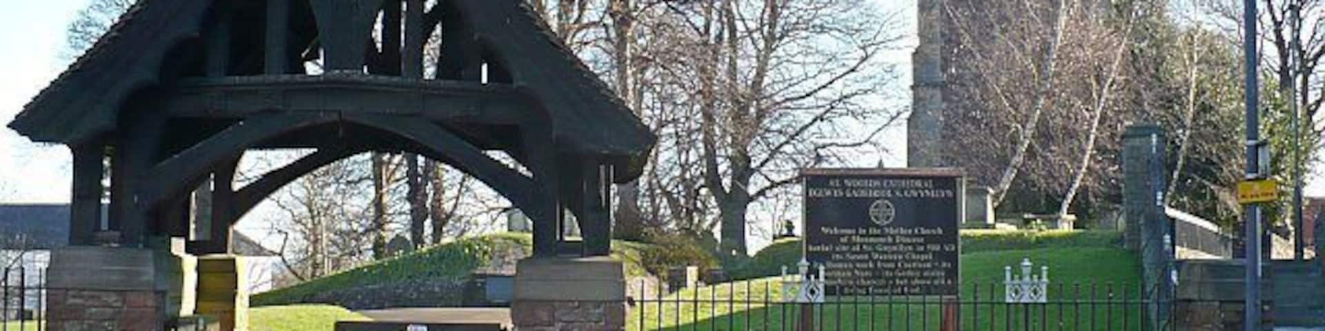 St Woolos Cathedral lychgate and tower The lychgate has two inscriptions. On the left "TO THE GLORY OF GOD THIS LYCHGATE AND WESTERN APPROACH WERE DEDICATED TO THE MEMORY OF DAVID HENRY GRIFFITHS M.A. ARCHDEACON OF MONMOUTH, VICAR OF ST WOOLOS A.D. 1908-1926". On the right "BLESSED IS THE MAN WHOM THOU CHOOSEST AND RECEIVEST UNTO THEE: HE SHALL DWELL IN THY COURTS AND SHALL BE SATISFIED WITH THE PLEASURES OF THY HOUSE".