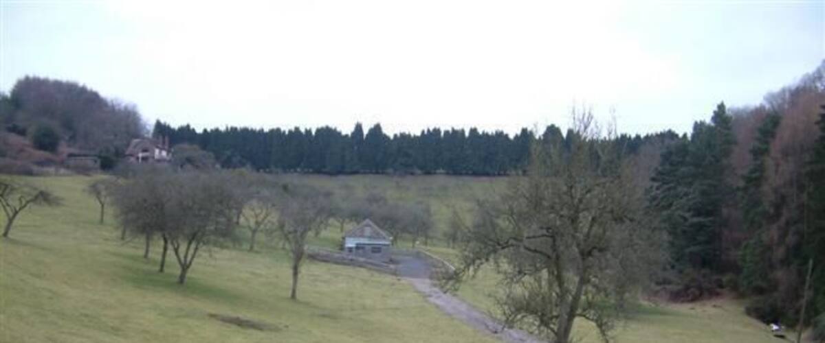 Un campo cubierto de césped con árboles y un edificio pequeño a lo lejos.