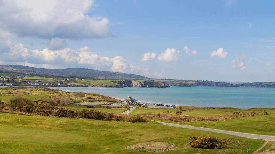 A coastal landscape with a golf course, a lighthouse, and cliffs.