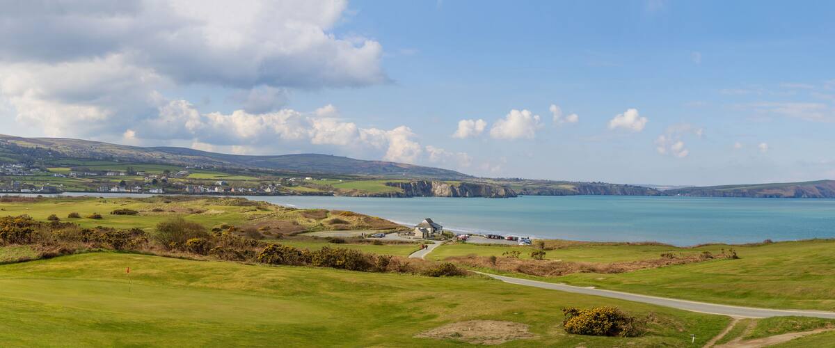 A coastal landscape with a golf course, a lighthouse, and cliffs.