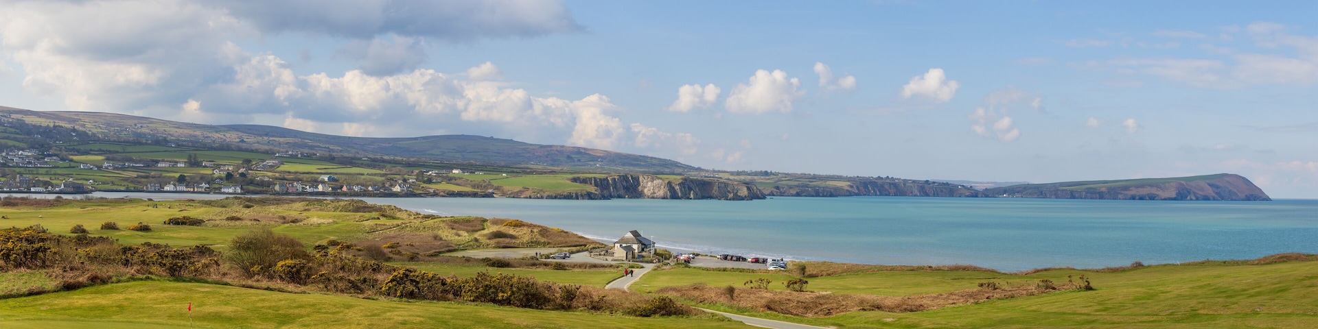 A coastal landscape with a golf course, a lighthouse, and cliffs.