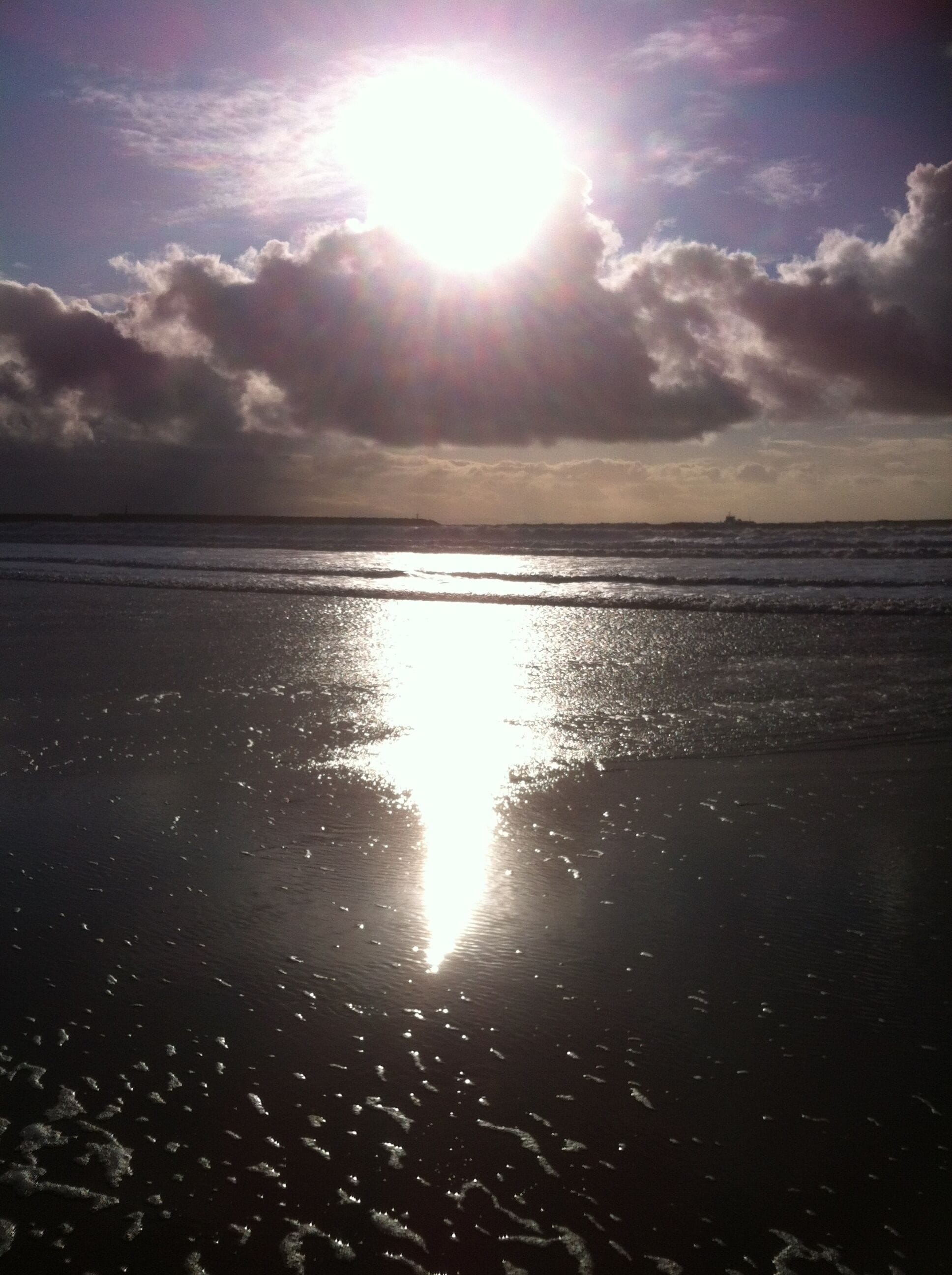 Una playa con la luz del sol reflejada en la arena húmeda y el océano.