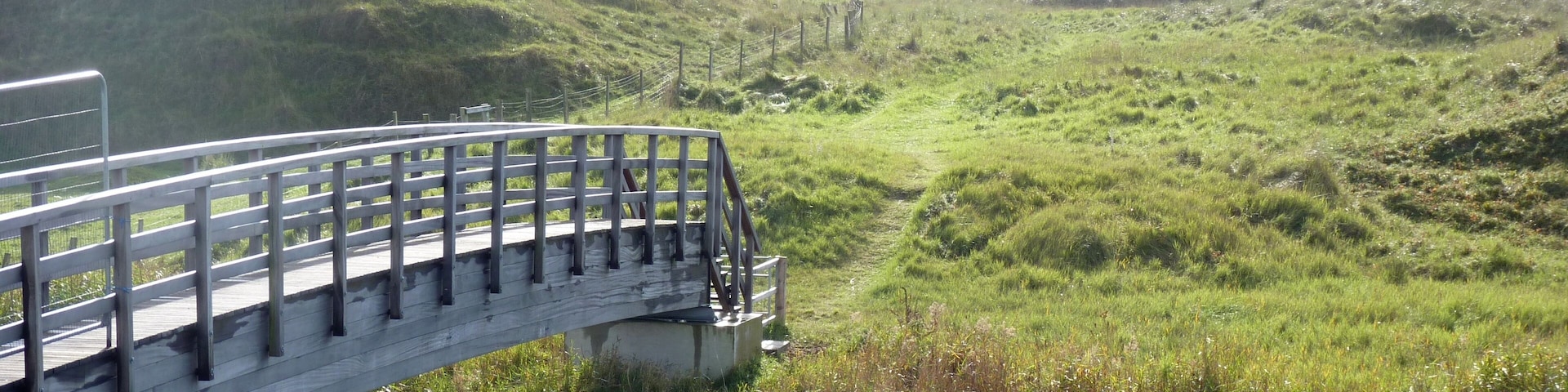 Looking east over a footbridge linking Neath Port Talbot and Bridgend stretches of the Wales Coast Path. The River Kenfig is the boundary, and is also point where the Gower and Swansea Bay section meets the South Wales and Severn Estuary section of the path. The path continues east through Kenfig Sands.